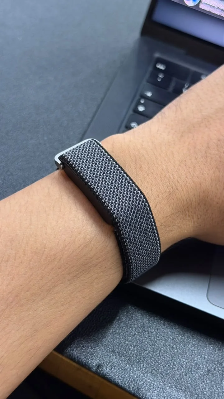 Mana on a wrist — a slim sensor in a brushed-metal frame on a dark woven band
